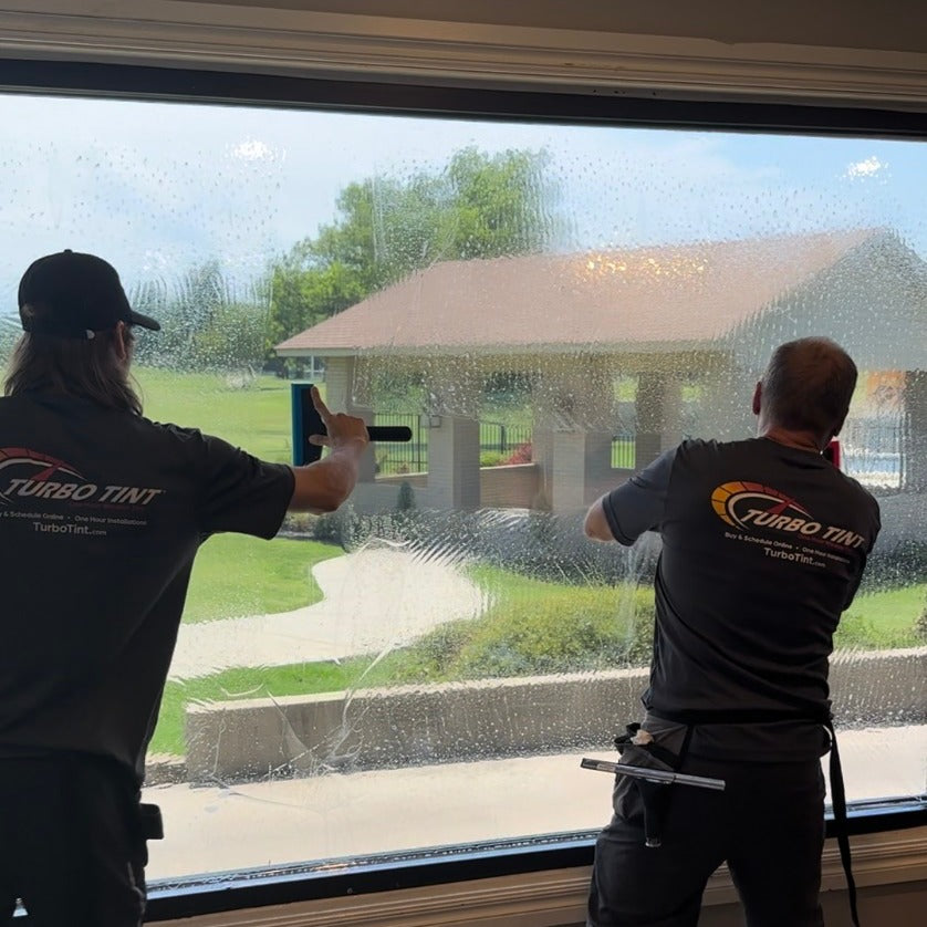 Two workers from Turbo Tint applying window tinting to a large glass window.